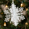 White 3D metal snowflake ornament hanging against dark Christmas tree greenery
